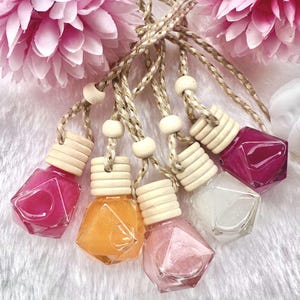 May include: Six colourful, geometric-shaped glass bottles with wooden stoppers and gold string hanging from them. The bottles are filled with different coloured liquids and glitter.