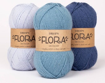 May include: Three skeins of DROPS FLORA yarn in light blue, blue, and grey. The yarn is made of alpaca and wool and is labeled "UNI COLOUR" and "Everyday comfort in alpaca and wool".
