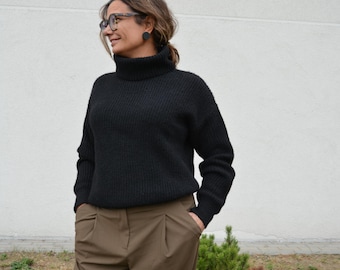May include: A black long-sleeve sweater with a ribbed turtleneck collar and ribbed cuffs, paired with olive green trousers featuring a pleated front design and side pockets. The sweater has a thick knit texture and a relaxed fit throughout.