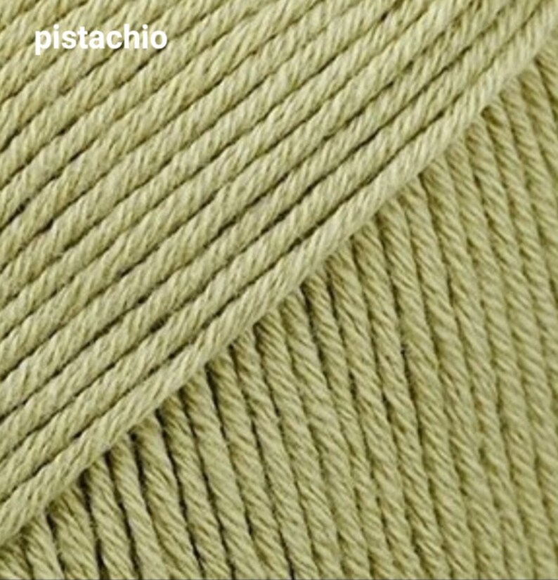 Puede incluir: Primer plano de una madeja de hilo de color pistacho. El hilo es suave y texturizado, con un brillo sutil.