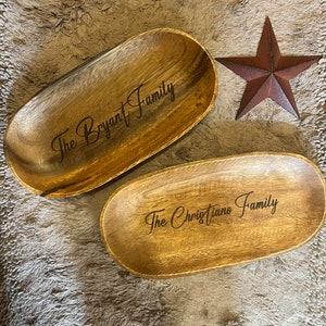 May include: Two wooden oval serving trays with engraved family names, "The Bryant Family" and "The Christiano Family". A rustic, reddish-brown star decorates the background. The trays are made of light brown wood.