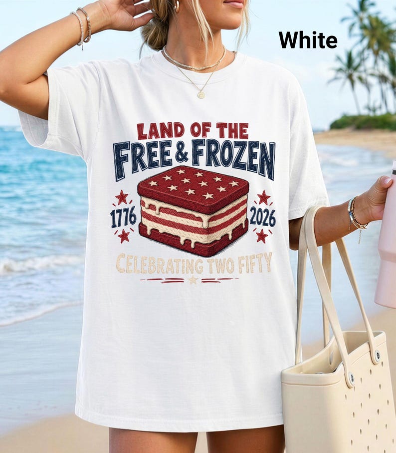 May include: A white short-sleeve t-shirt featuring a graphic of an ice cream sandwich with red and white stripes and stars. The text reads LAND OF THE FREE & FROZEN, 1776, 2026, and CELEBRATING TWO FIFTY. The design includes red stars and decorative lines.