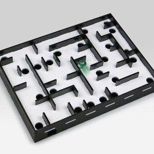 Può includere: Un gioco di labirinto in legno nero con una biglia verde all'interno. Il labirinto ha uno sfondo bianco e pareti nere.