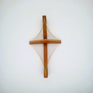 May include: A wooden cross with a geometric pattern created by string wrapped around it. The string is a light gold color and the wood is a dark brown.