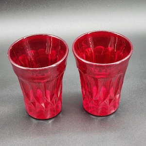 May include: Two red glass tumblers with a diamond pattern. The glasses are clear and have a slightly frosted appearance.
