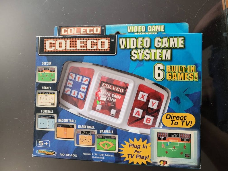 May include: A white and red Coleco Video Game System with six built-in games. The system has a joystick and buttons for playing games such as football, hockey, soccer, and basketball. The system connects directly to a TV.