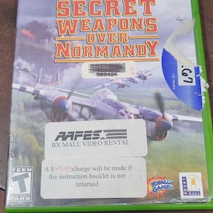 May include: A green Xbox game case for "Secret Weapons Over Normandy". The case has a picture of a plane flying over a field. The game is rated T for Teen by the ESRB. The case has a sticker that says "AAFES BX Mall Video Rental" and a warning that a $49.95 charge will be made if the instruction booklet is not returned.