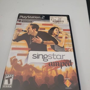 May include: A PlayStation 2 game case for SingStar Amped. The case is black with a red, white, and blue design. The game requires two microphones. The game is rated T for Teen by the ESRB.