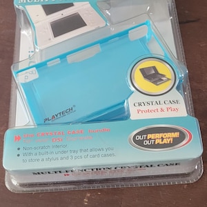 May include: A blue and white Nintendo DSi multi-function crystal case with a built-in tray for storing a stylus and 3 card cases. The packaging features the text "Playtech Outperform Outplay" and "Crystal Case Protect & Play".