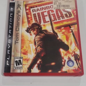 Puede incluir: Caja de juego de PlayStation 3 para Tom Clancy's Rainbow Six: Vegas. La portada presenta a un soldado con equipo t&aacute;ctico con el t&iacute;tulo del juego y la palabra "VEGAS" en letras grandes. La caja es roja.
