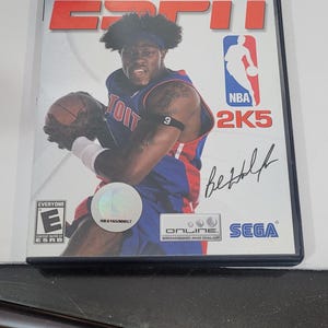 May include: A PlayStation 2 video game case for ESPN NBA 2K5. The cover features a basketball player in a blue jersey holding a basketball. The game is rated "Everyone" by the ESRB and includes the Sega logo.