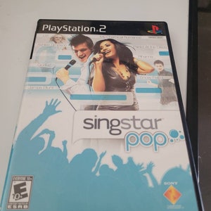 May include: A blue and white PlayStation 2 game case for SingStar Pop. The case features a silhouette of a crowd of people with their hands raised in the air. The game features songs by artists such as Gorillaz, Panic! At The Disco, and Rihanna.