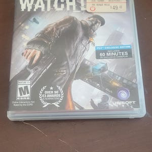 May include: A pre-owned PS3 game case for "Watch Dogs" featuring a man with a gun. The cover art is predominantly dark with a cityscape background. Includes "PS3 Exclusive Edition" with 60 minutes of gameplay.