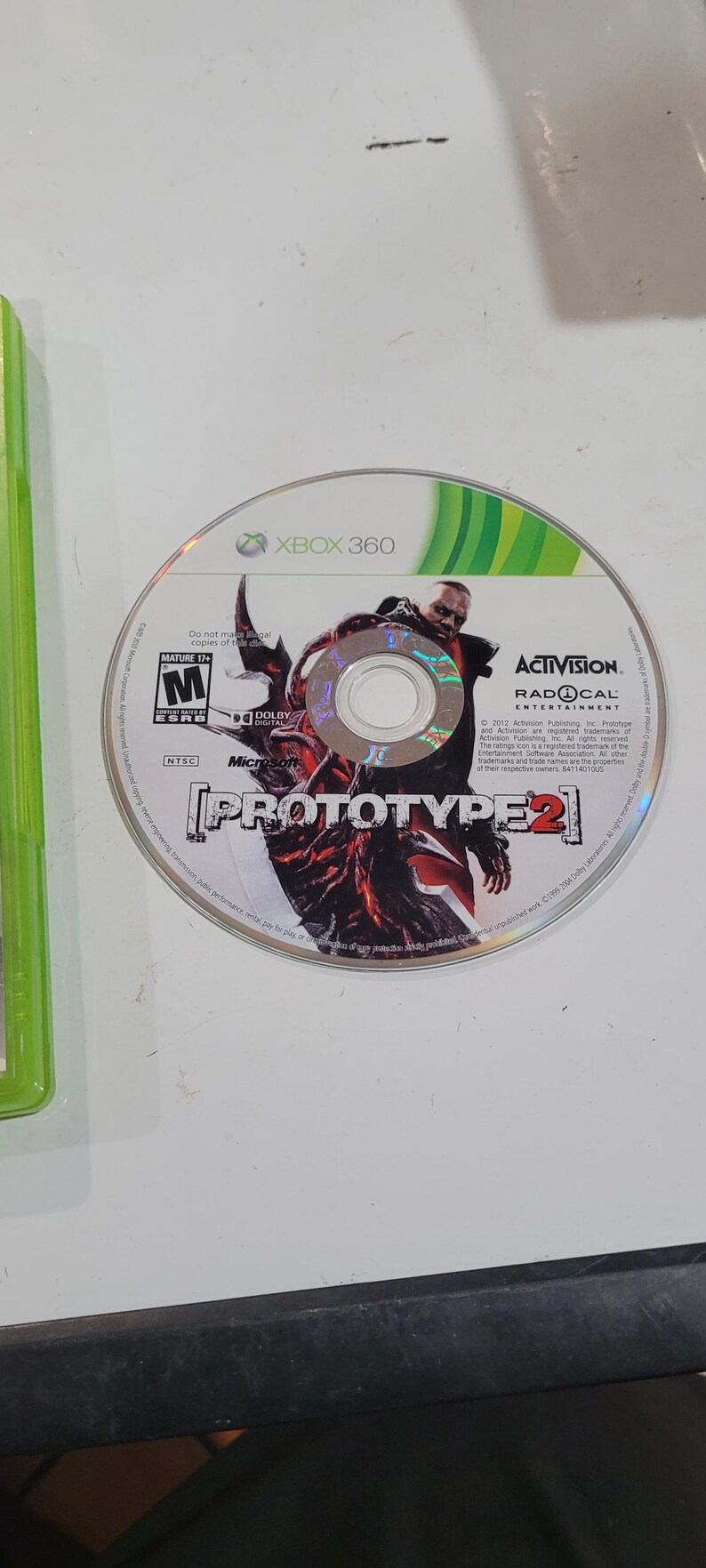 K&ouml;nnte beinhalten: Eine silberne Xbox 360-Spieledisc f&uuml;r Prototype 2, mit einem Charakter mit roten Augen und einem schwarzen und roten Outfit. Die Disc ist mit einer Altersfreigabe von 17+ versehen und wird von der ESRB bewertet. Das Spiel wird von Activision ver&ouml;ffentlicht und von Radical Entertainment entwickelt.