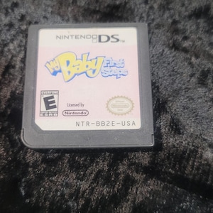 May include: Nintendo DS game cartridge for "My Baby First Steps". The game cartridge is black and gray with the game title in pink and blue. The ESRB rating is visible.
