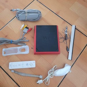 May include: A red and black Nintendo Wii console with a white remote, a white Wii MotionPlus controller, a white sensor bar, and various cables and accessories.