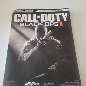 May include: A guide for the video game Call of Duty: Black Ops II. The cover features a soldier holding a gun, with the game title in large, bold letters. The guide is published by BradyGames and features the logos for Activision and Treyarch.