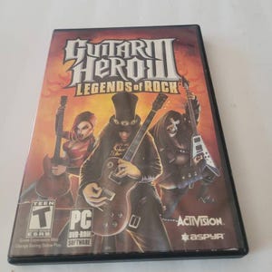 May include: A Guitar Hero III: Legends of Rock PC game case featuring a red, white, and blue background with three musicians playing electric guitars. The game is rated Teen by the ESRB.