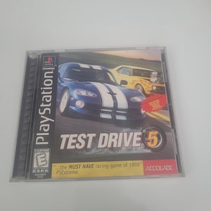 May include: A PlayStation game case for Test Drive 5, a racing game. The case is blue and features a blue and white sports car on the front. The text "...the MUST HAVE racing game of 1998" is printed on the front of the case.