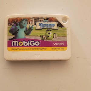 May include: A white plastic game cartridge for the VTech MobiGo. The cartridge features a pink background with the text "MobiGo" in white. The front of the cartridge has a picture of Mike and Sulley from the Disney Pixar movie Monsters University. The text "Disney/Pixar elements © 2013 Disney/Pixar 80-253100 (US)" is printed on the bottom of the cartridge.