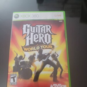 May include: Xbox 360 game case for Guitar Hero World Tour. The case is green and red with a picture of a band playing on stage. The game is rated T for Teen by the ESRB. The game is published by Activision.