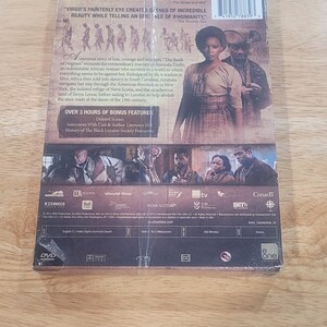 May include: DVD case for "The Book of Negroes" with a woman in a period costume on the cover. The back of the case includes text describing the film's plot and bonus features, with logos from various production companies.