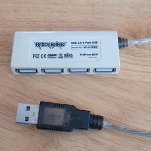 May include: A white Rockband USB 2.0 4-Port HUB with a black USB connector and a silver cable. The hub has four USB ports and the text "ROCKBAND" is visible.