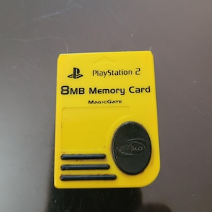May include: Yellow PlayStation 2 8MB Memory Card by MagicGate. The card has a black logo and a black circle with the letters "nko" inside.