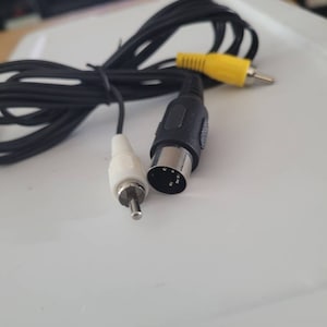 May include: Black AV cable with a yellow RCA connector, a white RCA connector, and a black connector with multiple pins. The cable is coiled and lies on a white surface.