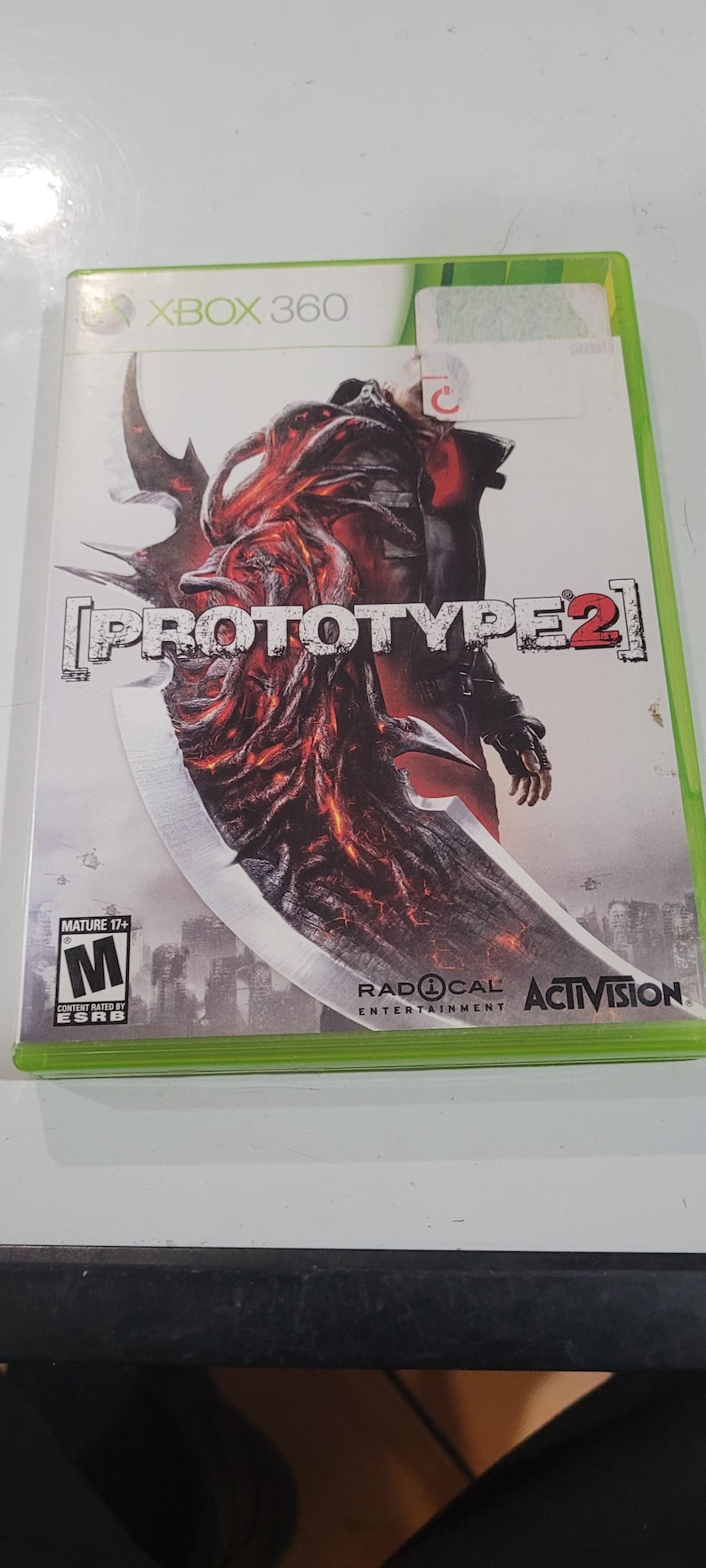 K&ouml;nnte beinhalten: Xbox 360-Spielecase f&uuml;r Prototype 2, mit einem roten und schwarzen Charakter mit einer gro&szlig;en Klinge vor wei&szlig;em Hintergrund. Das Spiel ist von der ESRB mit M f&uuml;r Mature bewertet. Das Spiel wird von Activision ver&ouml;ffentlicht und von Radical Entertainment entwickelt.