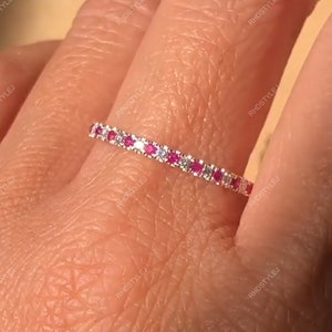 以下が含まれることがあります： 小さなピンクの宝石と、さらに小さな白い宝石が金属にセットされた、薄い銀のバンド