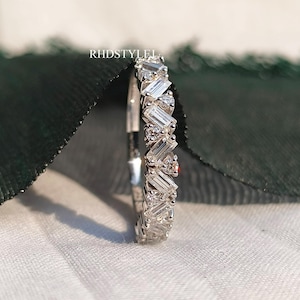 May include: A silver band ring with a row of baguette-shaped diamonds set in a staggered pattern.