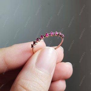 May include: A delicate gold band ring with a row of small, pink gemstones set in a curved pattern.