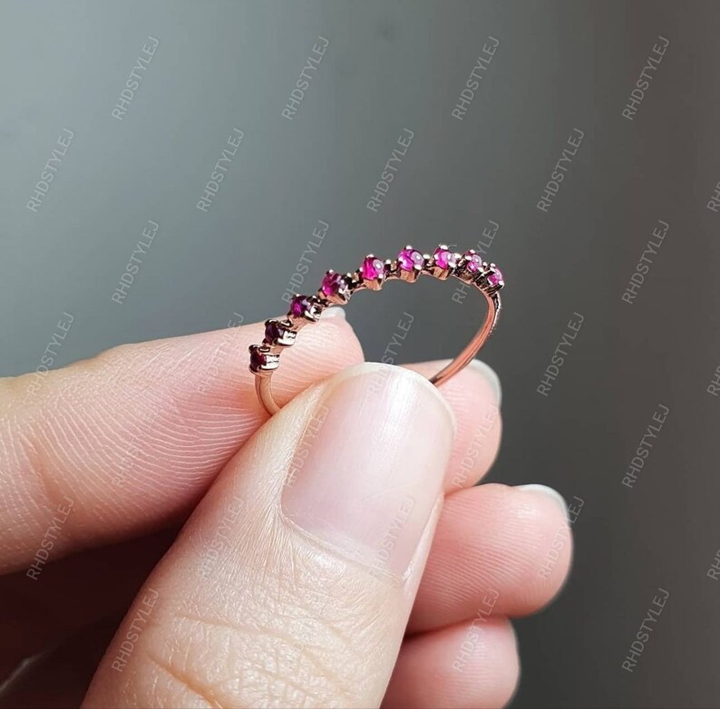May include: A delicate gold band ring with a row of small, pink gemstones set in a curved pattern.