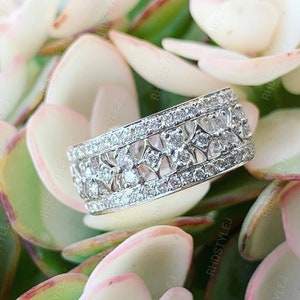 Op de afbeelding: Een zilveren bandring met een delicaat, ingewikkeld ontwerp met meerdere rijen kleine, glinsterende diamanten.