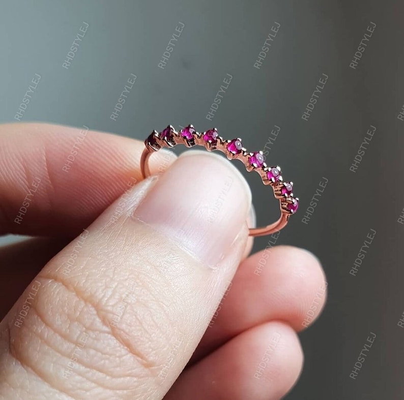May include: A delicate rose gold band ring with a row of small, sparkling pink gemstones.