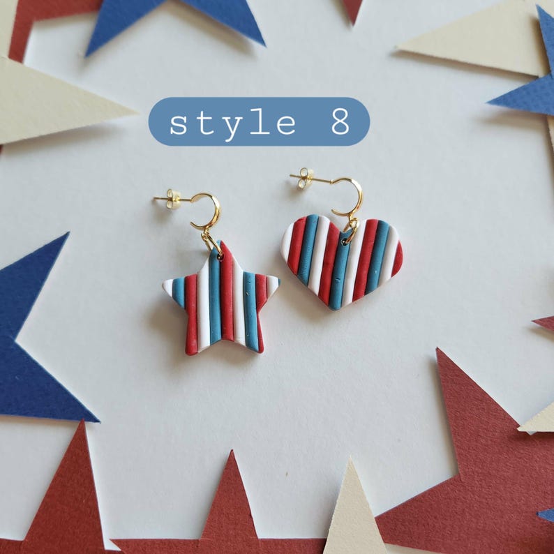 May include: A pair of mismatched earrings labeled style 8, featuring one star-shaped and one heart-shaped pendant. Both pendants display vertical stripes in red, white, and blue, suspended from small gold-toned hoops with post backings.