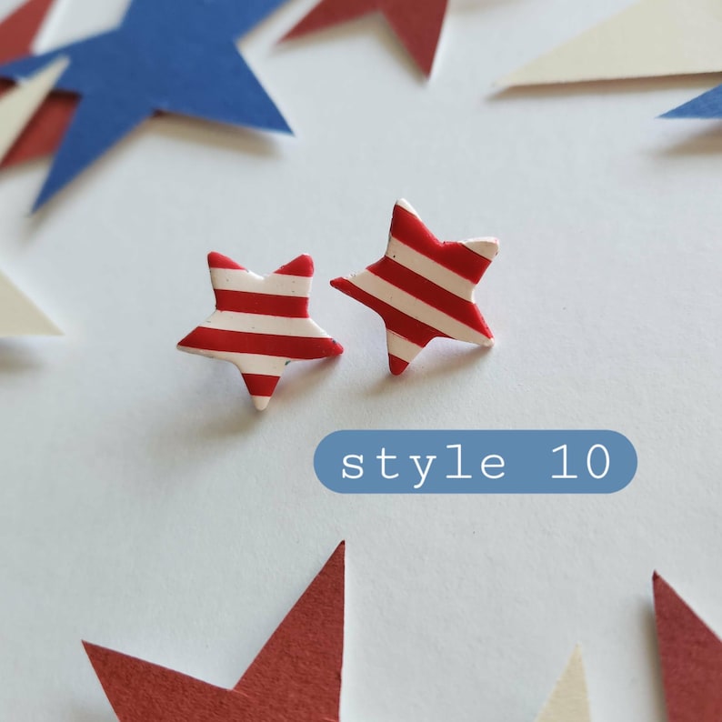 May include: A pair of star-shaped stud earrings featuring horizontal red and white stripes. The earrings are positioned above a blue rectangular graphic containing the white text style 10. The design consists of five-pointed stars with a smooth finish.