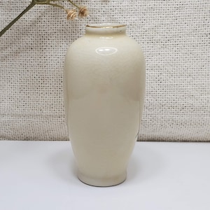 K&ouml;nnte beinhalten: Eine kleine, cremefarbene Keramikvase mit strukturierter Oberfl&auml;che und goldfarbenem Rand.