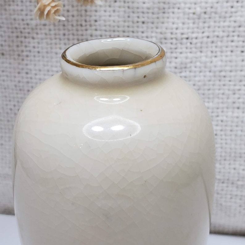 K&ouml;nnte beinhalten: Eine kleine, wei&szlig;e Keramikvase mit goldfarbenem Rand. Die Vase hat eine strukturierte Oberfl&auml;che und ist perfekt f&uuml;r die Pr&auml;sentation einer einzelnen Blume.