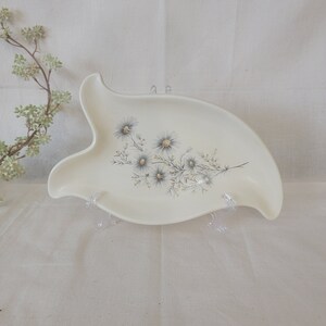 May include: A white ceramic serving dish with a floral design. The dish is shaped like a fish and has a raised edge. The flowers are blue and white and have a delicate, hand-painted look.