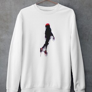 May include: White sweatshirt with a black silhouette of a person in a red hat jumping with paint dripping from them.