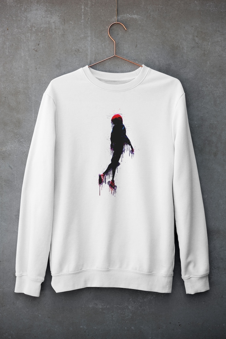 May include: White sweatshirt with a black silhouette of a person in a red hat jumping with paint dripping from them.