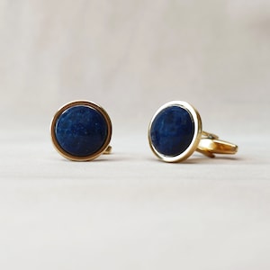 Op de afbeelding: Een paar gouden manchetknopen met blauwe stenen.