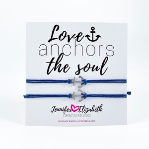 May include: Two blue friendship bracelets with silver anchor charms. The card reads "Love anchors the soul" and "Jennifer Elizabeth Design Studio Handmade Jewelry, Accessories & Gifts".