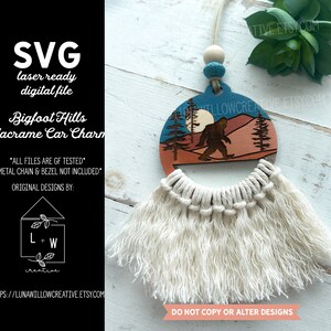 May include: A wooden Bigfoot Hills macrame car charm with a blue, orange, and brown design. The charm features a silhouette of Bigfoot walking in a forest setting with a full moon in the sky. The charm is attached to a white macrame tassel.