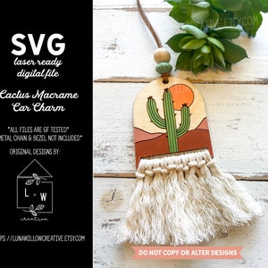 Op de afbeelding: Een houten cactus autohanger met een macramé kwast. De hanger is geschilderd met een groene cactus, een rode zonsondergang en een bruin woestijnlandschap. De tekst "NIET KOPIËREN OF WIJZIGEN VAN ONTWERPEN" staat onderaan de afbeelding.