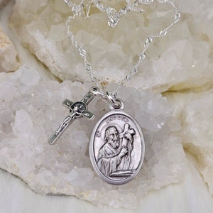 May include: A silver necklace featuring a pendant with the image of St. Andrew and a small crucifix. The oval pendant has the name "ANDREW" at the top. The chain is a delicate, twisted design.