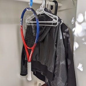 Puede incluir: Una raqueta de tenis roja, blanca y azul colgada de un gancho en un armario. La raqueta es de la marca Head y tiene el texto "Graphene 360+ Speed MP".