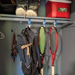 Puede incluir: Un armario blanco con una nevera roja, dos pares de botas de esqu&iacute; blancas y negras, una mochila azul, dos raquetas de tenis y un mosquet&oacute;n con una cuerda colgando de un gancho.